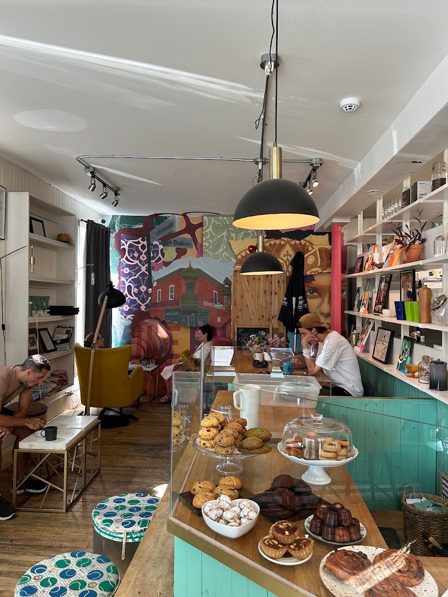 Intérieur chaleureux du Saint Louis café : comptoir turquoise, murale, viennoiseries et clients au travail.